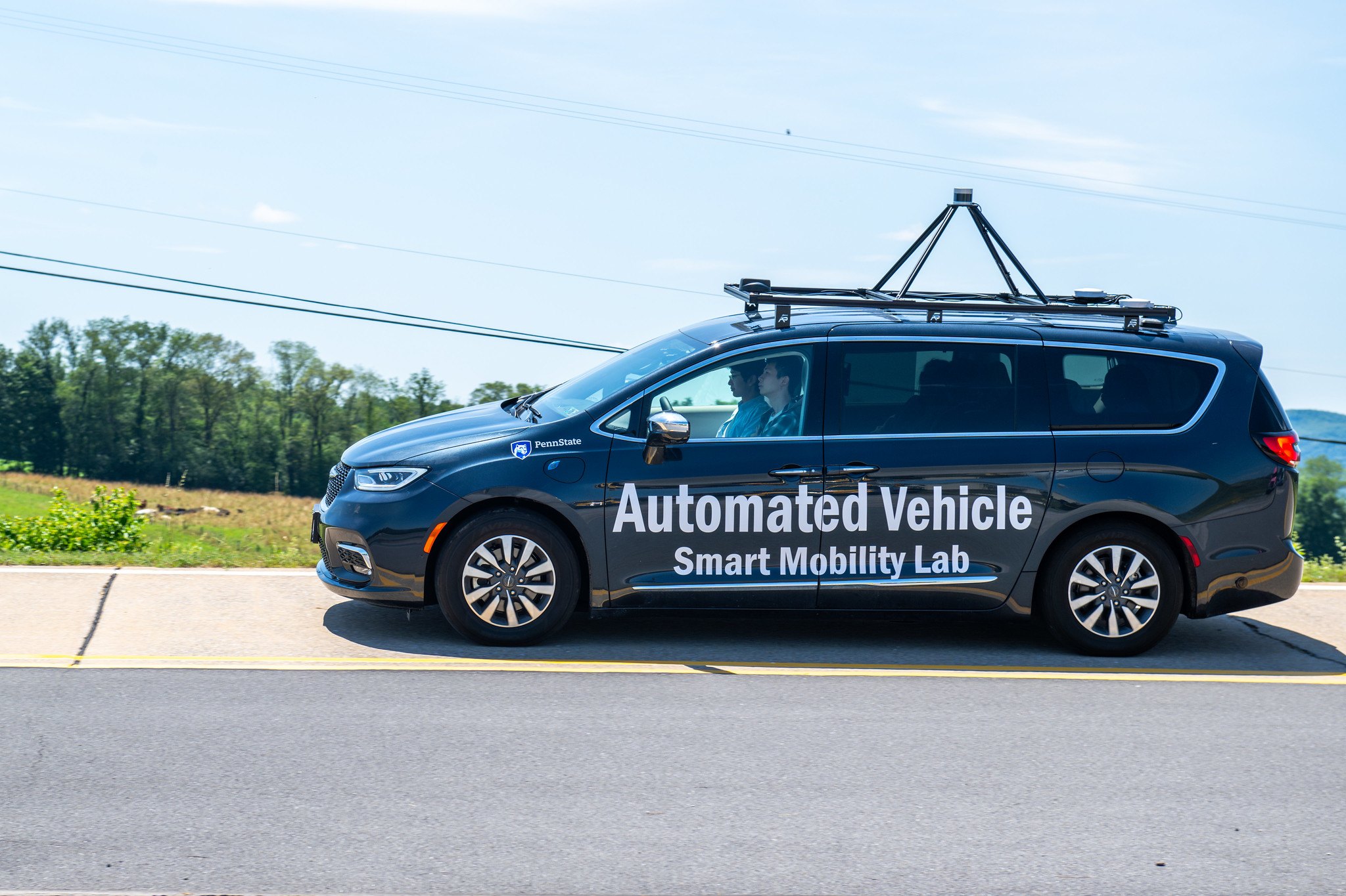 The Smart Mobility Lab's automated vehicle, a wrapped Chrysler Pacifica with a roof sensor rack, driving on the LTI test track